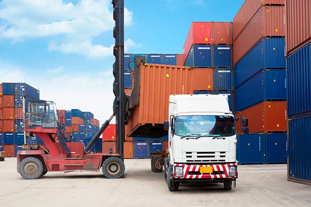 A shipping container being loaded onto a truck in a dock 