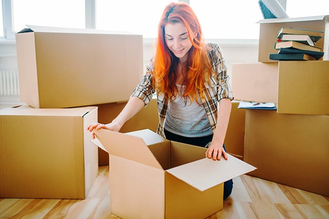 Young female college student excitedly opening a cardboard box to move in to her new dormroom