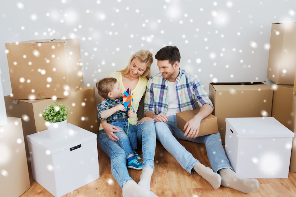 Young family of three sitting on the floor surrounded by unopened cardboard boxes